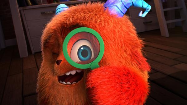Das kleine, orangefarbene Monster Gary hält sich Beas Lupe vor das Auge.