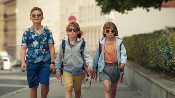 Drei Kinder laufen nebeneinander auf einem Fußweg. Sie tragen Sonnenbrillen und versuchen einen coolen Eindruck zu machen.