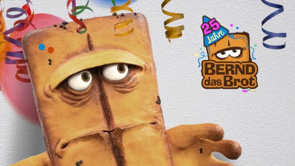 Bernd das Brot blickt skeptisch zu einem Logo von Bernd das Brot mit Party-Hütchen, auf dem die Zahl 25 steht. Hinter ihm weiße Rauhfasertapete. Von oben hängen Luftschlangen herab.