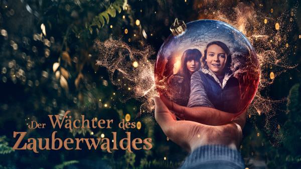 Rechts eine ausgestreckte Hand, die eine Glaskugel hält. Darin sind die Gesichter von Luca und Tala. Im Hintergrund Tannengrün und Lichter. Unten der Titel Der Wächter des Zauberwaldes.