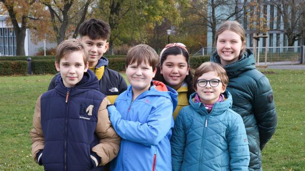 Der Kinderredaktionsrat mit Michael, Margarete und Johanna, Jonathan, Nils und Maggy steht eng beieinander auf einer Wiese auf dem Gelände des Landesfunkhauses in Erfurt. 