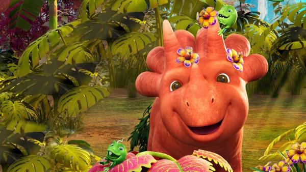 Ginger ähnelt einem Triceratops-Saurier. Blüten sind auf ihren Hörnern und sie schaut freundlich. Um sie herum ist eine urzeitliche Vegetation und vorne auf einem Blatt ein winziger Erbs-Rex.