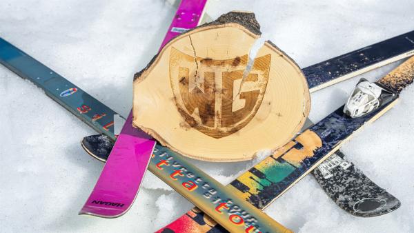 Um eine Holzscheibe mit dem Logo der WG liegen Skibretter quer durcheinander im Schnee.