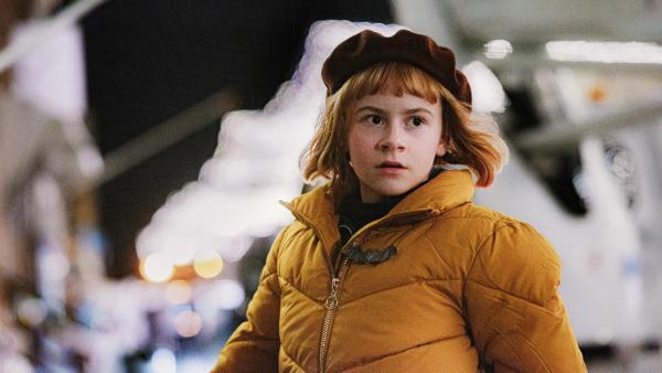 Nelly mit Blick in die Ferne. Sie ist mit einer Winterjacke und Mütze bekleidet.