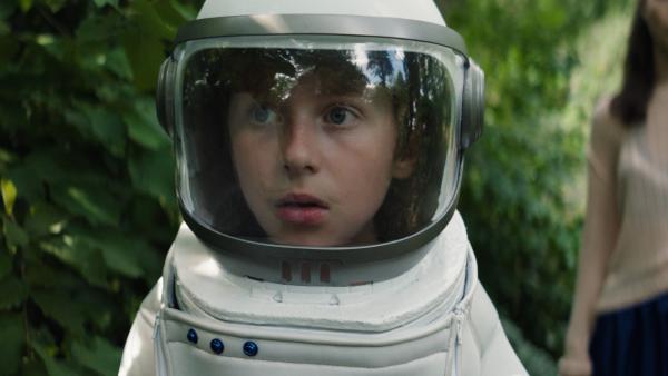 Tom (Theo Kretschmer) steht im Garten mit seinem Astronautenanzug.